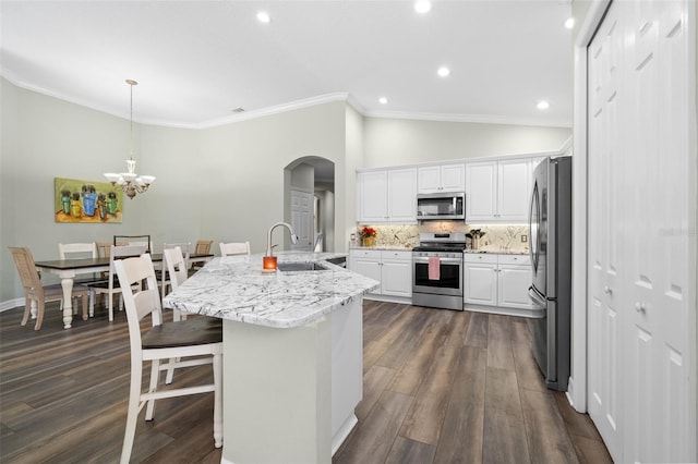 kitchen featuring a breakfast bar, hanging light fixtures, an island with sink, stainless steel appliances, and white cabinets