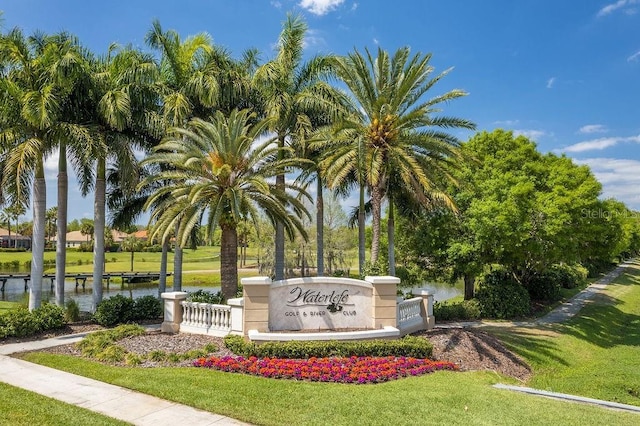 community / neighborhood sign featuring a lawn and a water view