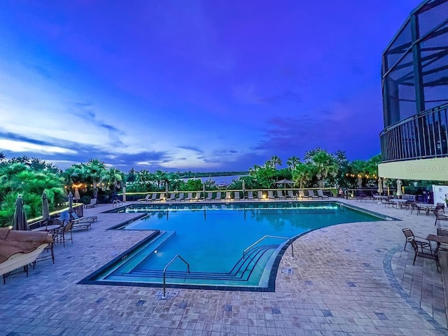 pool at dusk featuring a patio area and glass enclosure