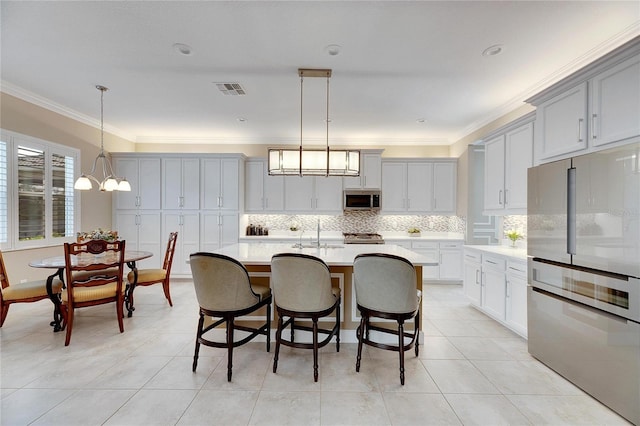 kitchen featuring stainless steel appliances, crown molding, an inviting chandelier, hanging light fixtures, and an island with sink