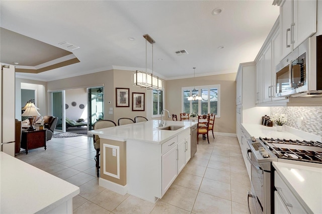 kitchen featuring a kitchen island with sink, sink, appliances with stainless steel finishes, decorative light fixtures, and white cabinetry