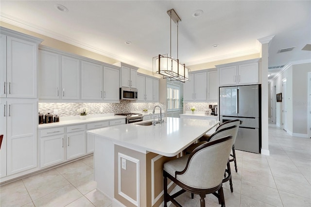 kitchen with a kitchen island with sink, sink, crown molding, appliances with stainless steel finishes, and decorative light fixtures