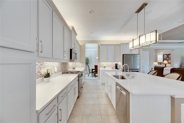 kitchen featuring appliances with stainless steel finishes, sink, light tile patterned floors, decorative light fixtures, and a center island with sink