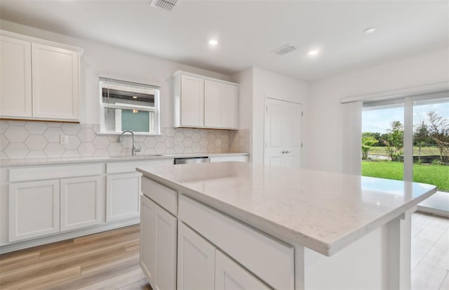 kitchen with decorative backsplash, sink, light hardwood / wood-style flooring, white cabinets, and a kitchen island