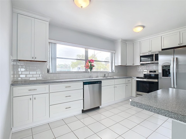 kitchen featuring appliances with stainless steel finishes, backsplash, sink, light tile patterned floors, and white cabinetry