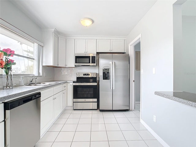 kitchen featuring appliances with stainless steel finishes, backsplash, sink, light tile patterned floors, and white cabinets