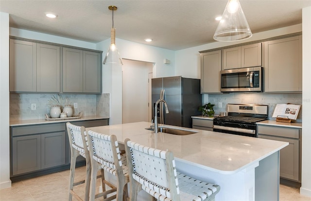 kitchen featuring gray cabinets, a center island with sink, stainless steel appliances, and decorative light fixtures