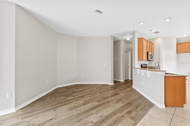 kitchen featuring kitchen peninsula, a breakfast bar, light hardwood / wood-style flooring, and stone countertops