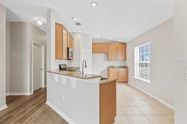 kitchen with lofted ceiling, stone counters, sink, kitchen peninsula, and stainless steel appliances