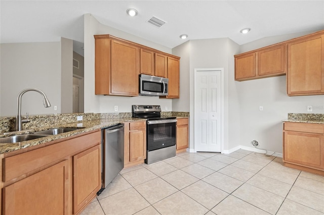 kitchen with light stone countertops, appliances with stainless steel finishes, vaulted ceiling, sink, and light tile patterned flooring