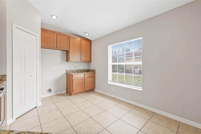 kitchen featuring light stone countertops, light tile patterned floors, vaulted ceiling, and range