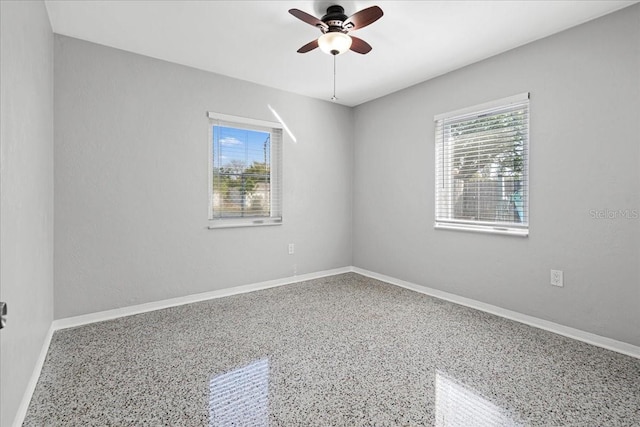 empty room with a ceiling fan, speckled floor, and baseboards