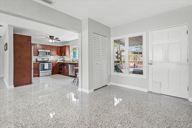 kitchen featuring baseboards, open floor plan, light countertops, stainless steel appliances, and light speckled floor