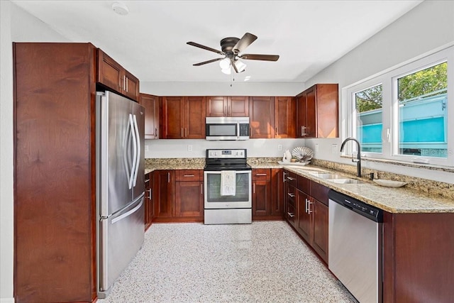 kitchen with a sink, light stone countertops, appliances with stainless steel finishes, and ceiling fan