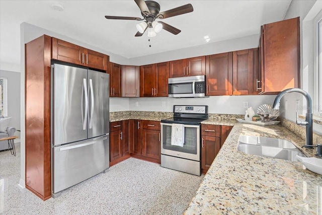 kitchen featuring a sink, light stone counters, light speckled floor, stainless steel appliances, and ceiling fan