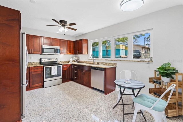 kitchen with dark brown cabinets, light stone countertops, appliances with stainless steel finishes, and a sink