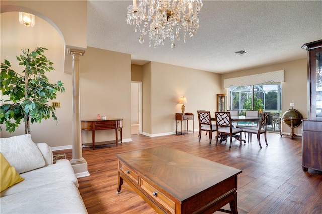 living room with hardwood / wood-style floors, a notable chandelier, ornate columns, and a textured ceiling