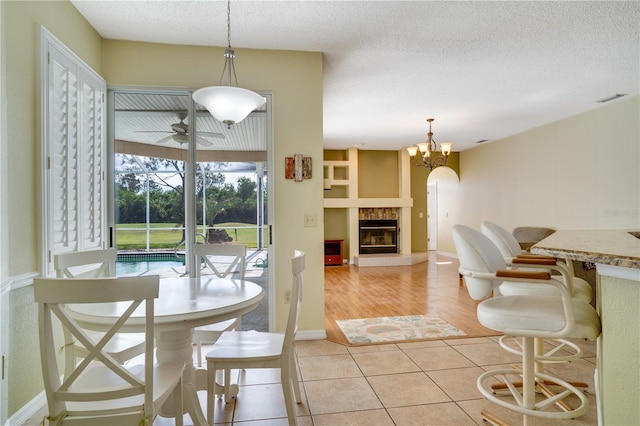 dining room with a tile fireplace, a textured ceiling, light hardwood / wood-style floors, and ceiling fan with notable chandelier