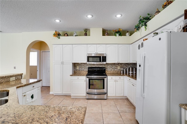 kitchen featuring white cabinets, light tile patterned floors, a textured ceiling, appliances with stainless steel finishes, and light stone counters