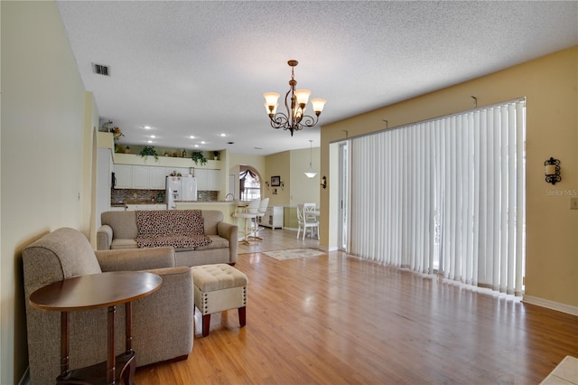 living room with a textured ceiling, light wood-type flooring, and a notable chandelier