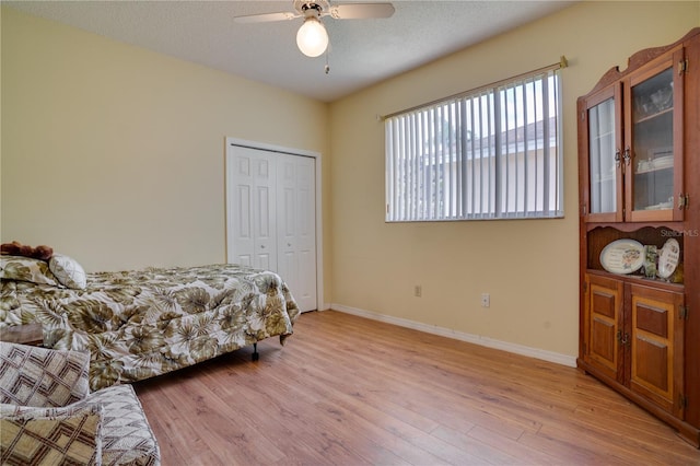 bedroom with a textured ceiling, a closet, light hardwood / wood-style flooring, and ceiling fan