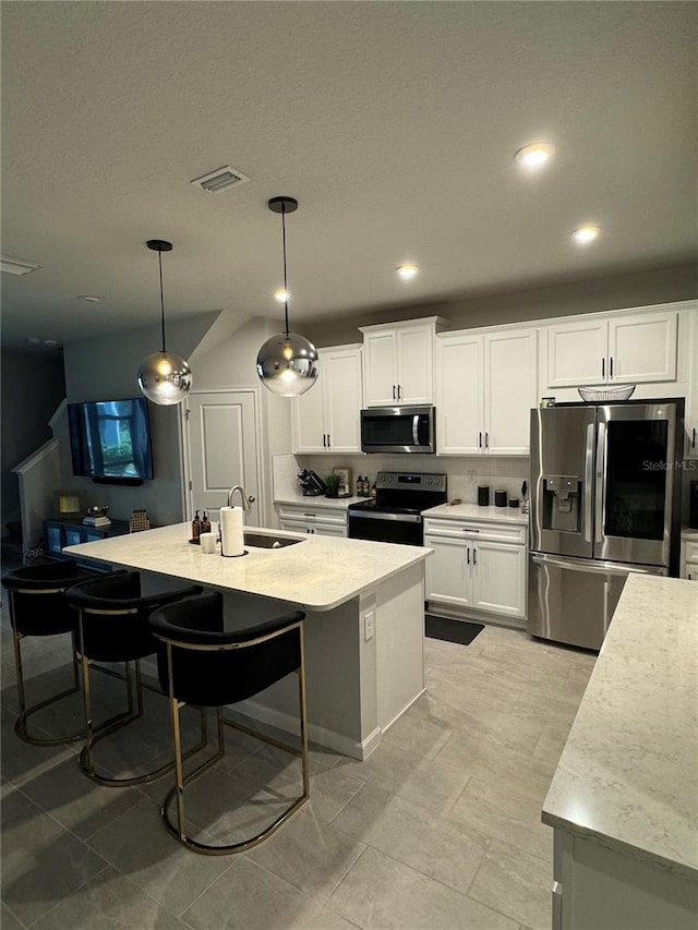 kitchen with stainless steel appliances, a kitchen island with sink, sink, decorative light fixtures, and white cabinetry