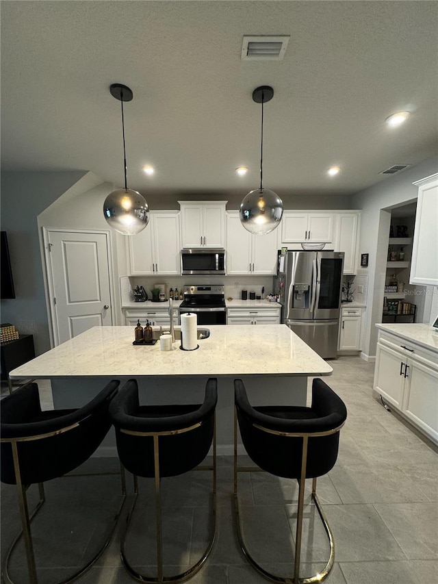 kitchen featuring pendant lighting, light stone countertops, stainless steel appliances, and an island with sink