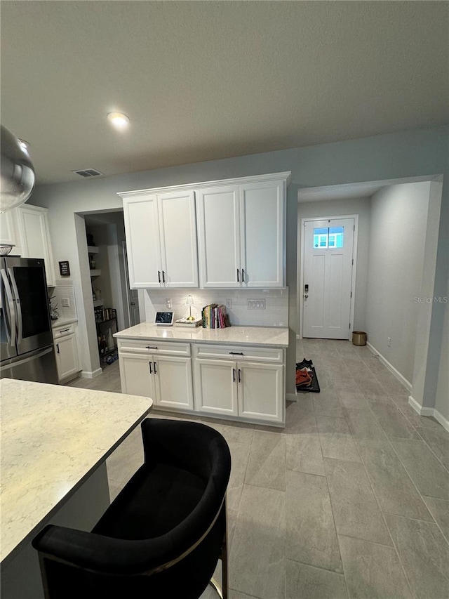 kitchen featuring decorative backsplash, stainless steel fridge, and white cabinetry