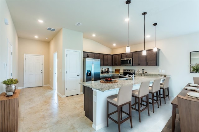 kitchen featuring light stone countertops, hanging light fixtures, stainless steel appliances, a kitchen breakfast bar, and kitchen peninsula