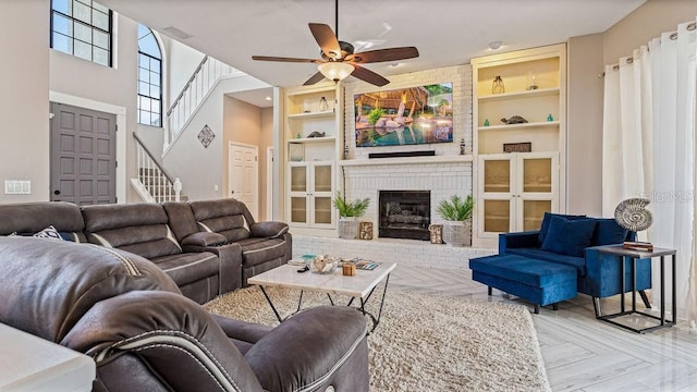 living room featuring a towering ceiling, a brick fireplace, light parquet floors, ceiling fan, and built in features