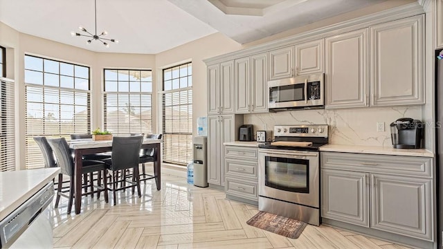 kitchen featuring decorative backsplash, appliances with stainless steel finishes, a wealth of natural light, and a notable chandelier