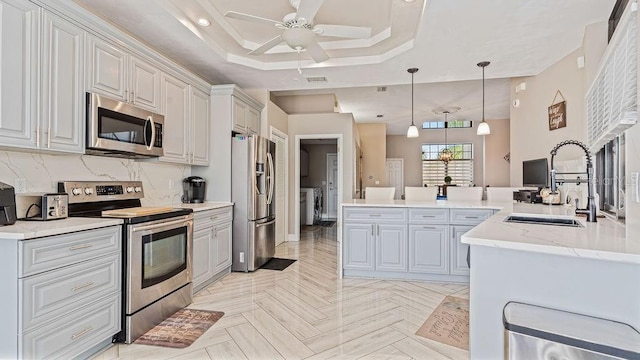 kitchen with stainless steel appliances, a tray ceiling, ceiling fan, sink, and pendant lighting