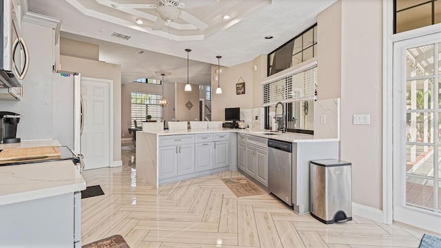 kitchen with kitchen peninsula, a tray ceiling, pendant lighting, dishwasher, and gray cabinets