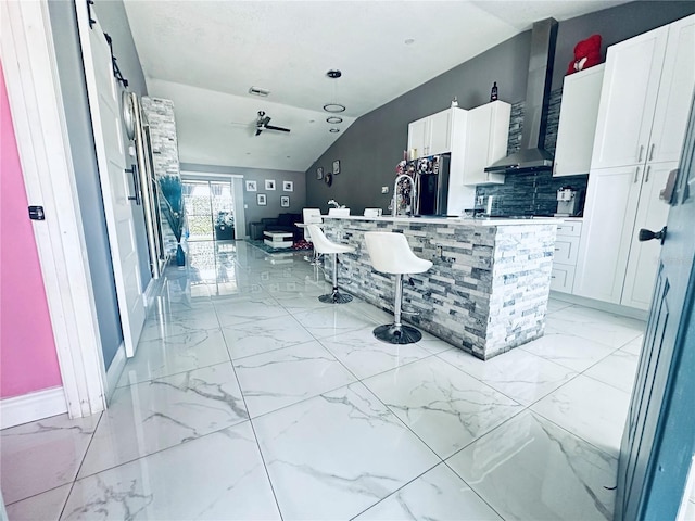 kitchen featuring white cabinets, ceiling fan, wall chimney exhaust hood, and vaulted ceiling