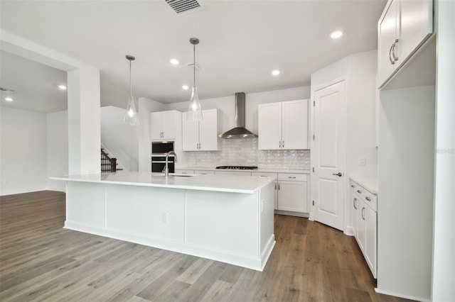 kitchen with wall chimney exhaust hood, decorative light fixtures, a kitchen island with sink, and white cabinets