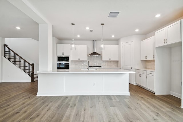 kitchen with wall chimney exhaust hood, sink, white cabinetry, decorative light fixtures, and wall oven