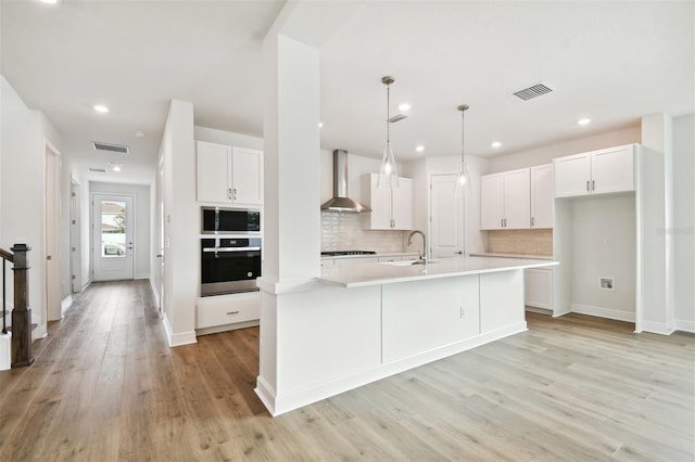 kitchen with a center island with sink, white cabinets, wall chimney range hood, and oven