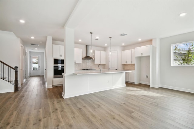 kitchen with wall chimney exhaust hood, oven, a center island with sink, and white cabinets