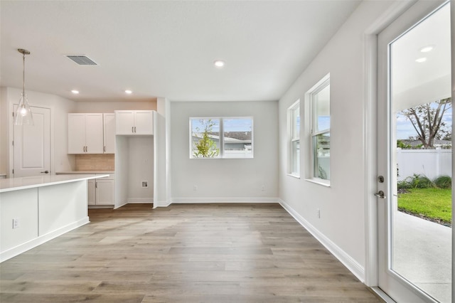 interior space featuring white cabinetry, decorative light fixtures, light wood-type flooring, and backsplash