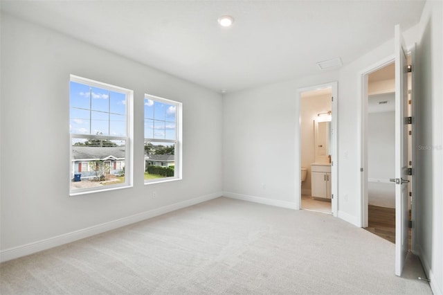 unfurnished bedroom featuring light colored carpet and ensuite bathroom