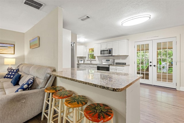 kitchen featuring kitchen peninsula, french doors, a breakfast bar, stainless steel appliances, and white cabinets