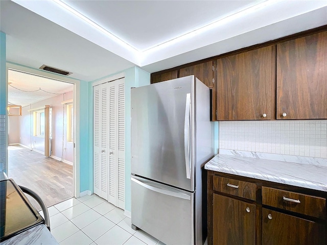 kitchen with stove, light tile patterned floors, tasteful backsplash, dark brown cabinets, and stainless steel refrigerator