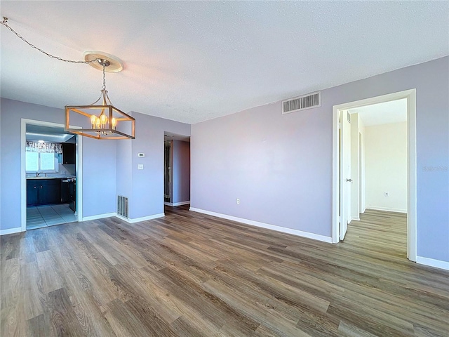 unfurnished living room featuring sink, dark wood-type flooring, a textured ceiling, and a notable chandelier