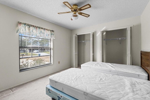 carpeted bedroom with a textured ceiling, two closets, and ceiling fan