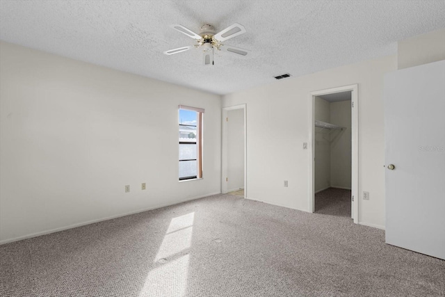 unfurnished bedroom featuring a textured ceiling, carpet floors, a spacious closet, and ceiling fan