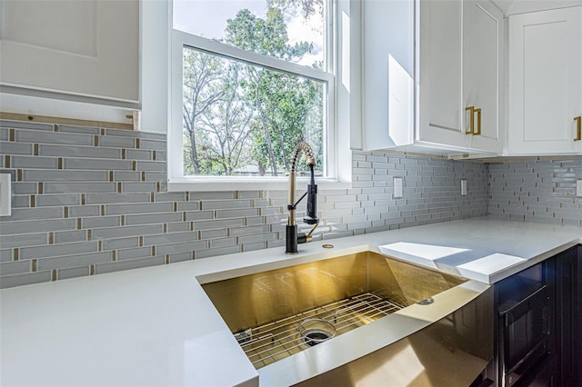 kitchen with tasteful backsplash, light countertops, white cabinetry, and a sink