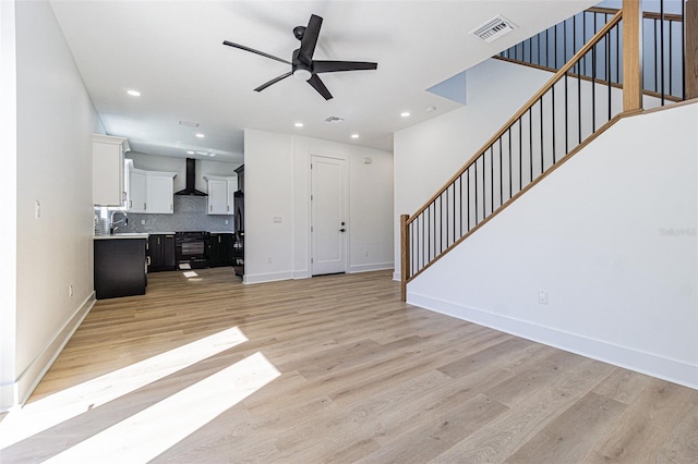 living room featuring visible vents, stairway, light wood-style flooring, a ceiling fan, and baseboards