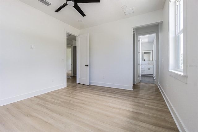 unfurnished bedroom featuring connected bathroom, wood finished floors, a ceiling fan, visible vents, and baseboards