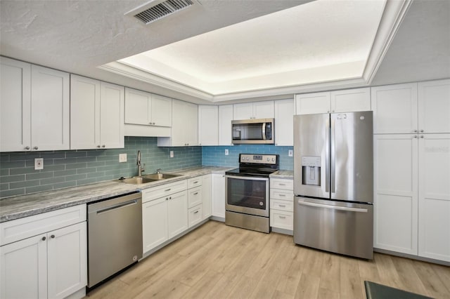 kitchen featuring appliances with stainless steel finishes, a tray ceiling, sink, light hardwood / wood-style flooring, and white cabinetry