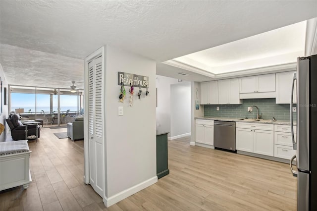 kitchen with light wood-type flooring, expansive windows, stainless steel appliances, sink, and white cabinetry